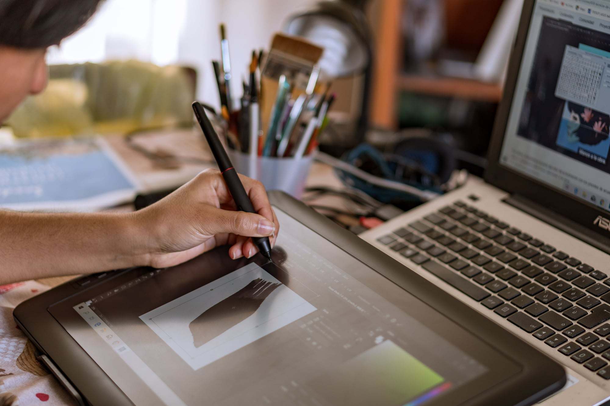 Een ontwerper tekent op een pentablet naast een laptop