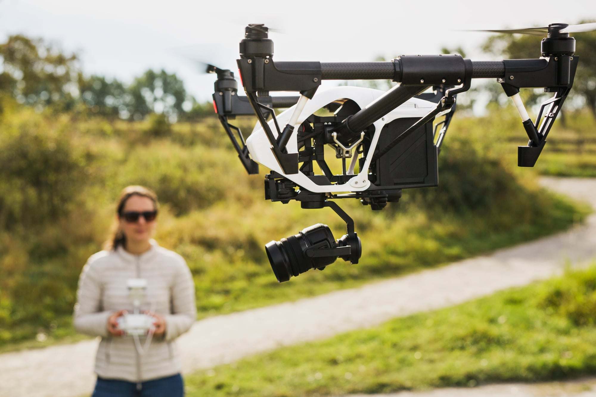 Een cameradrone in de lucht, met de piloot op de achtergrond