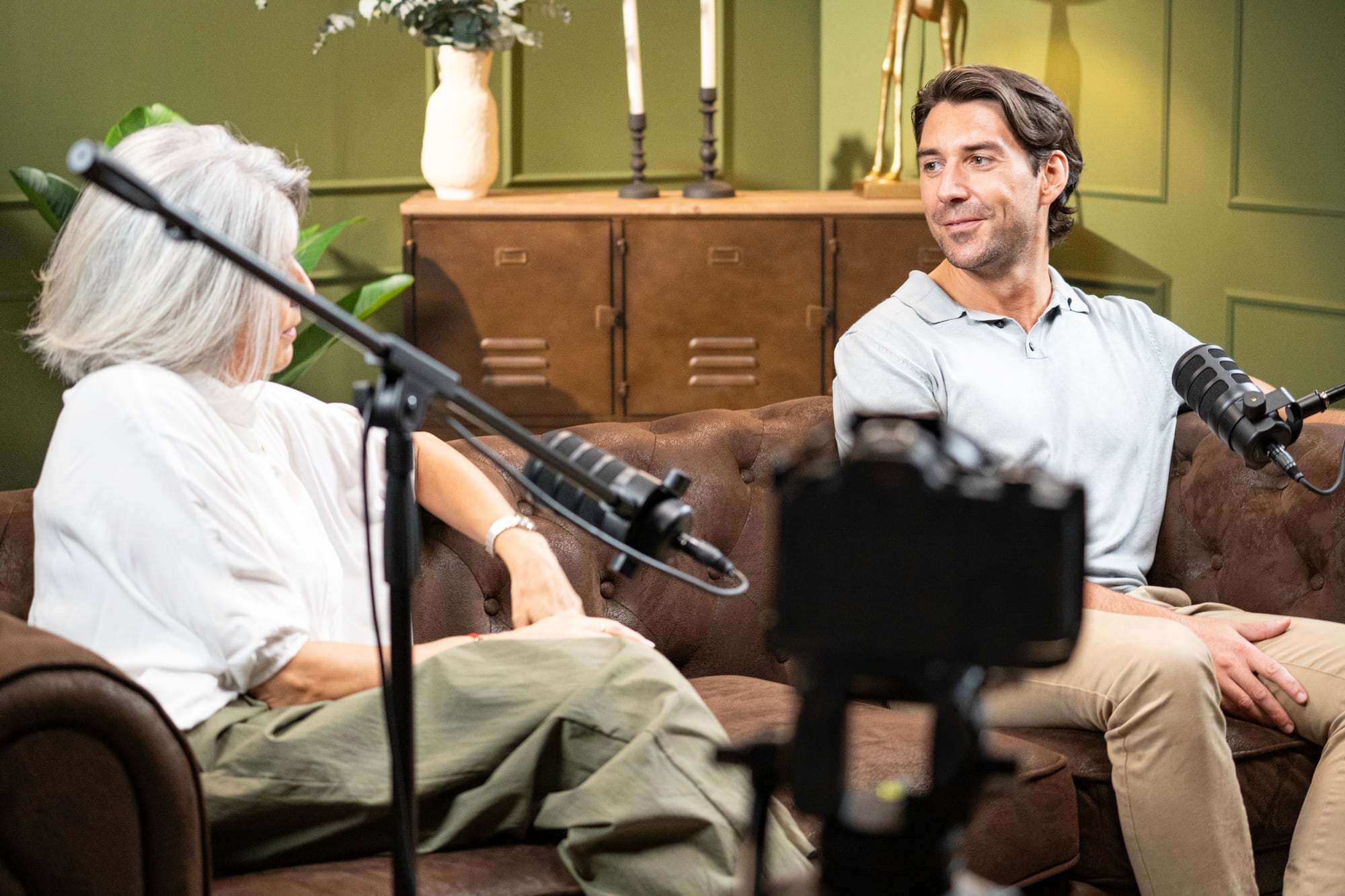 Twee mensen nemen op een bank een podcastinterview op met microfoons en een camera