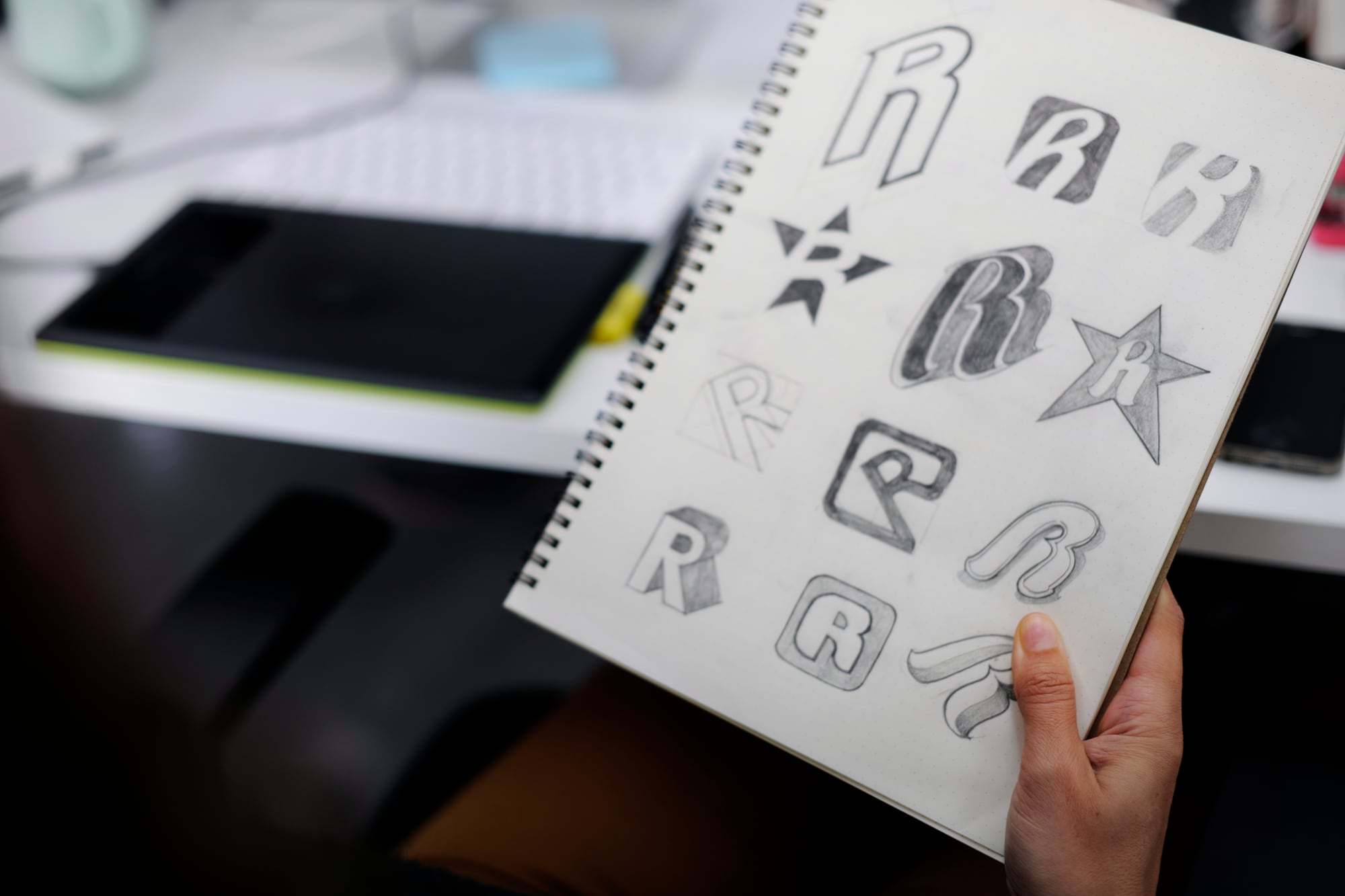 Een schetsboek met logo-ontwerpen boven een bureau
