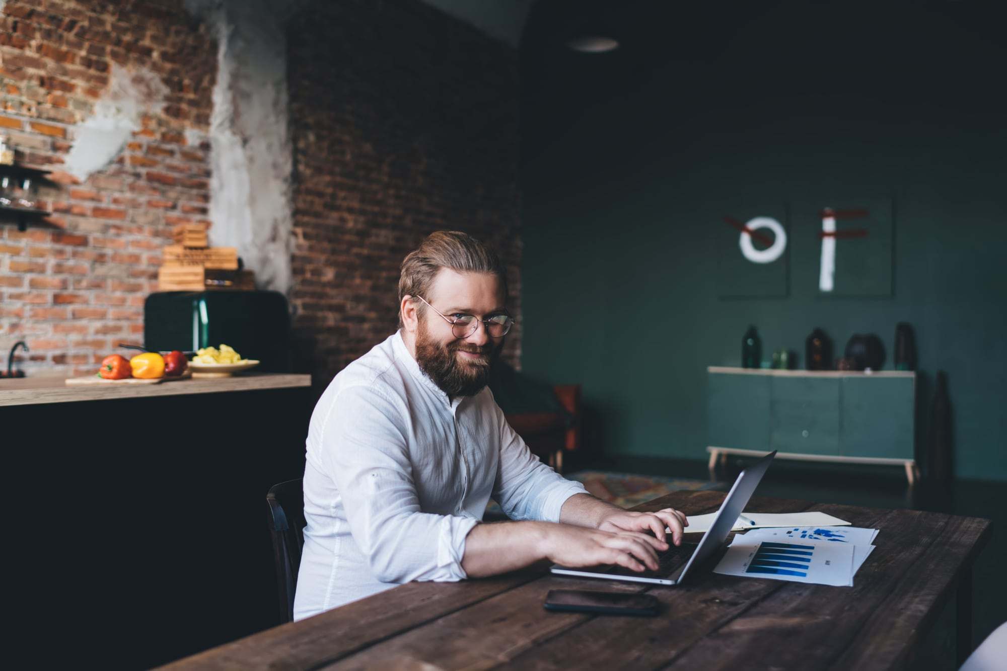 Een webdesigner werkt op een laptop aan een grote houten tafel