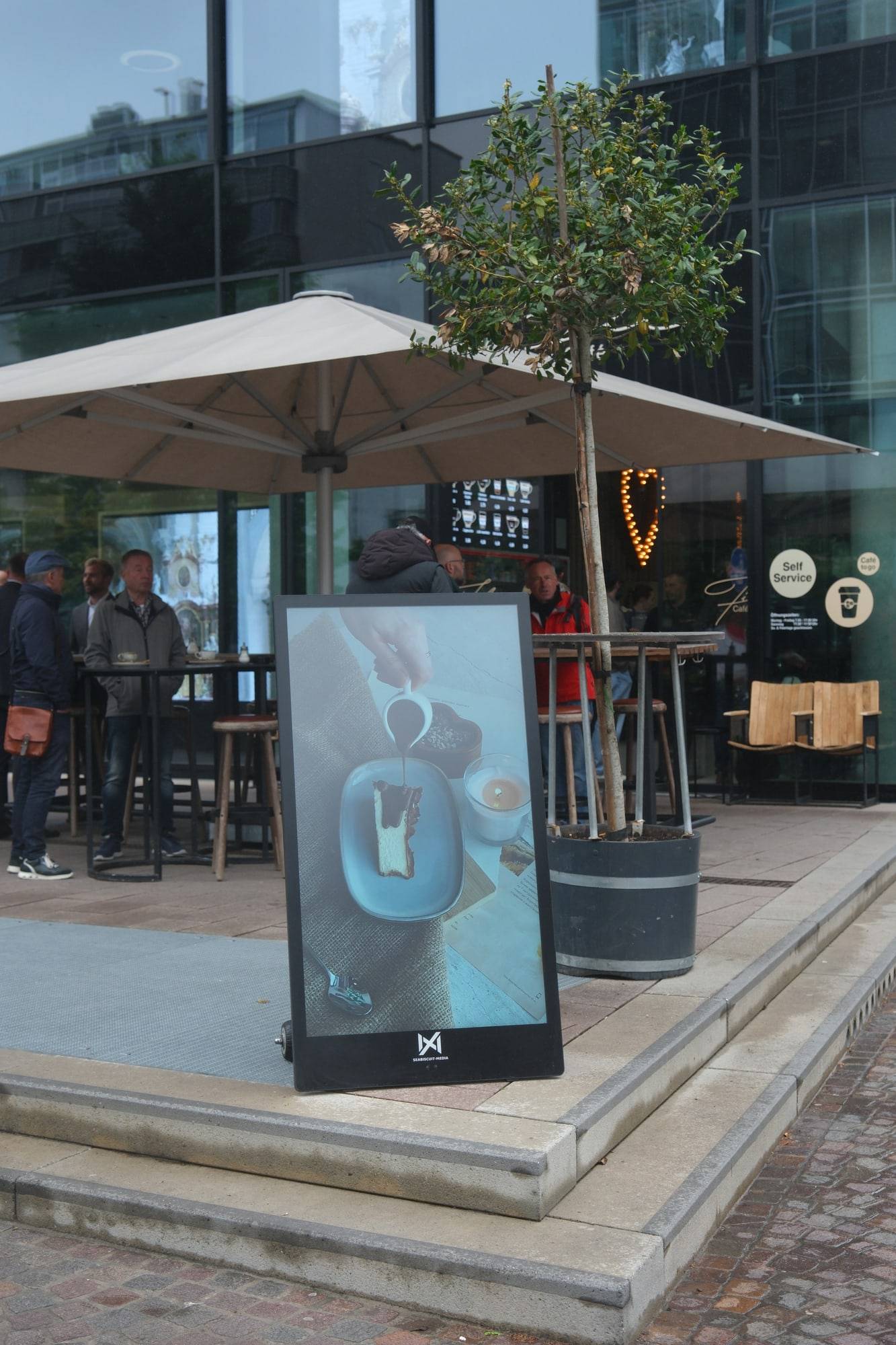 Seabiscuit-buitenscherm naast een caféterras onder een grote parasol