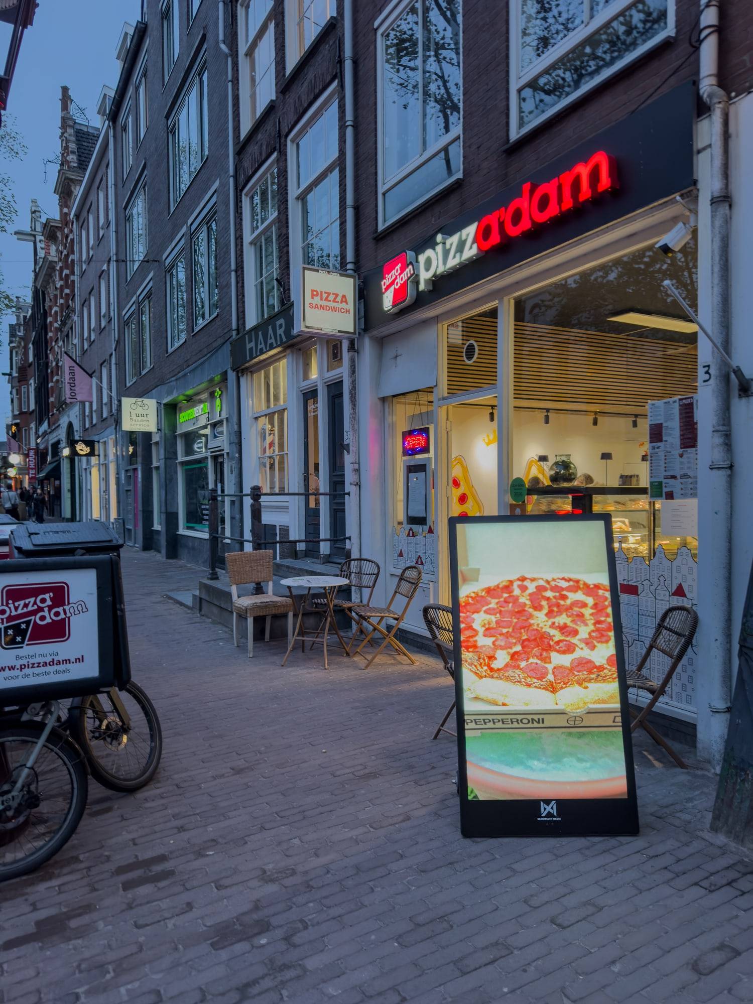 Seabiscuit-buitenscherm met een pizza-advertentie voor een restaurant in Amsterdam bij schemering